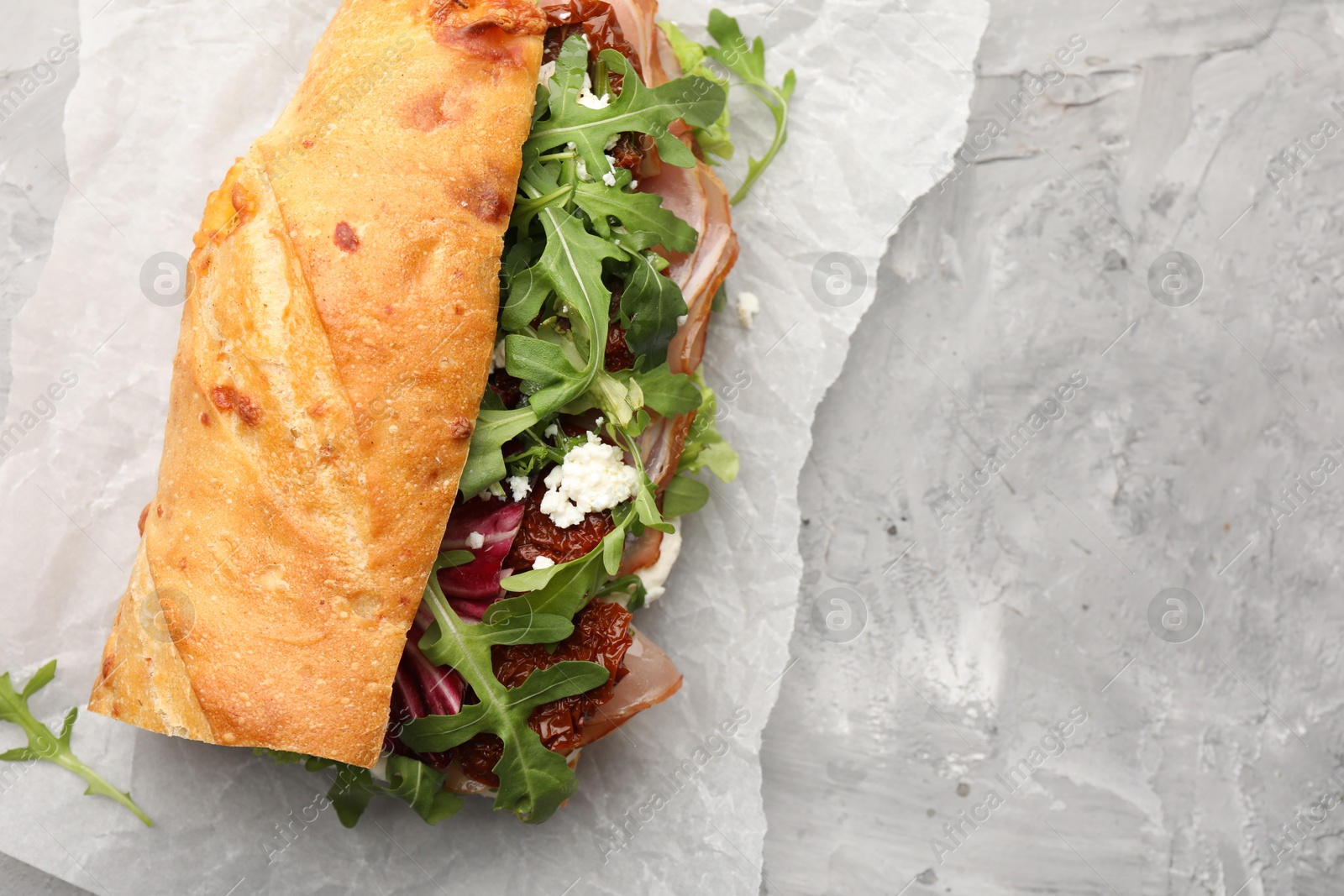 Photo of Baguette sandwich with ham and sun dried tomatoes on grey textured table, top view. Space for text