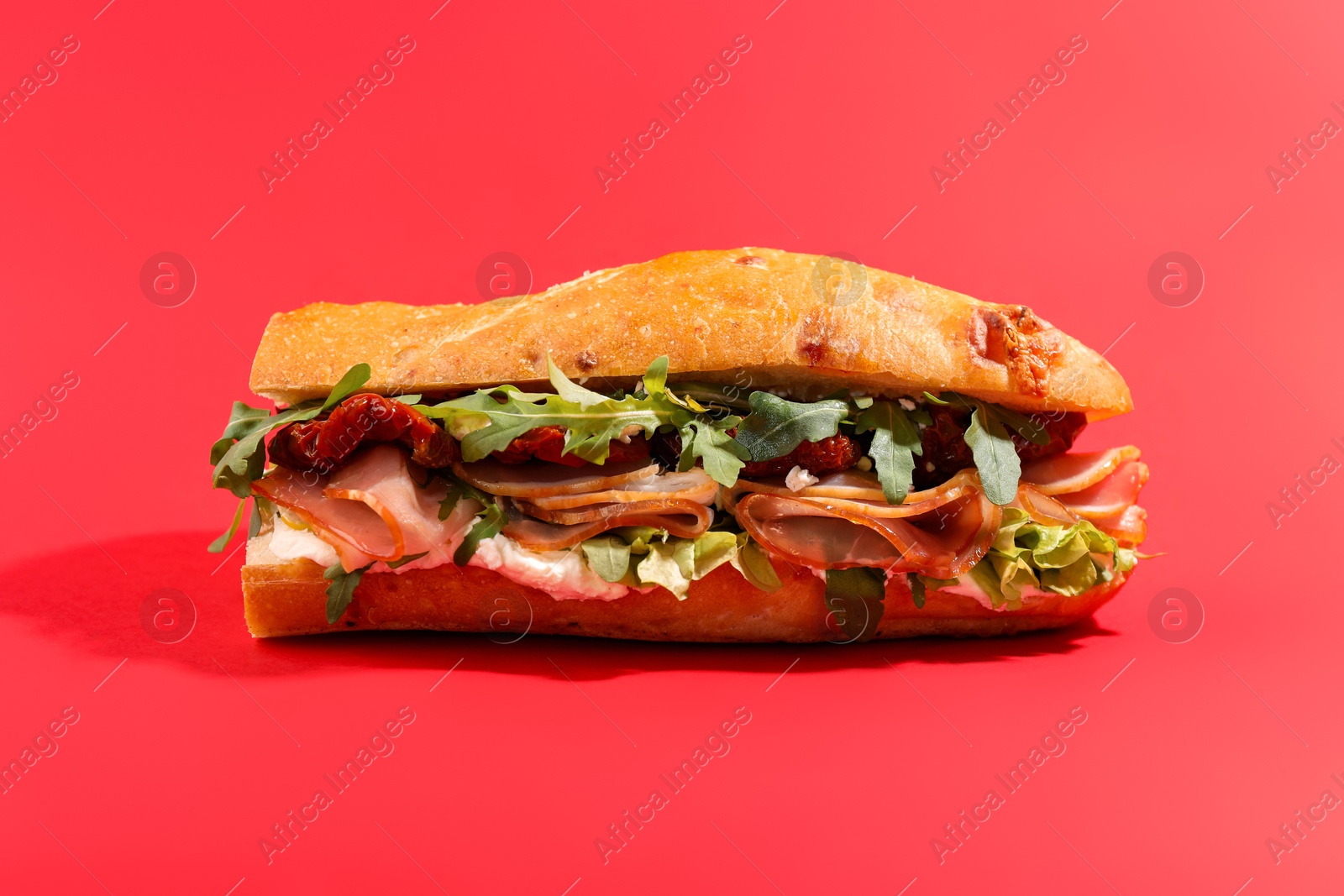 Photo of Baguette sandwich with ham and sun dried tomatoes on red background