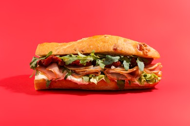 Photo of Baguette sandwich with ham and sun dried tomatoes on red background