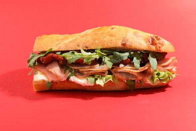 Photo of Baguette sandwich with ham and sun dried tomatoes on red background