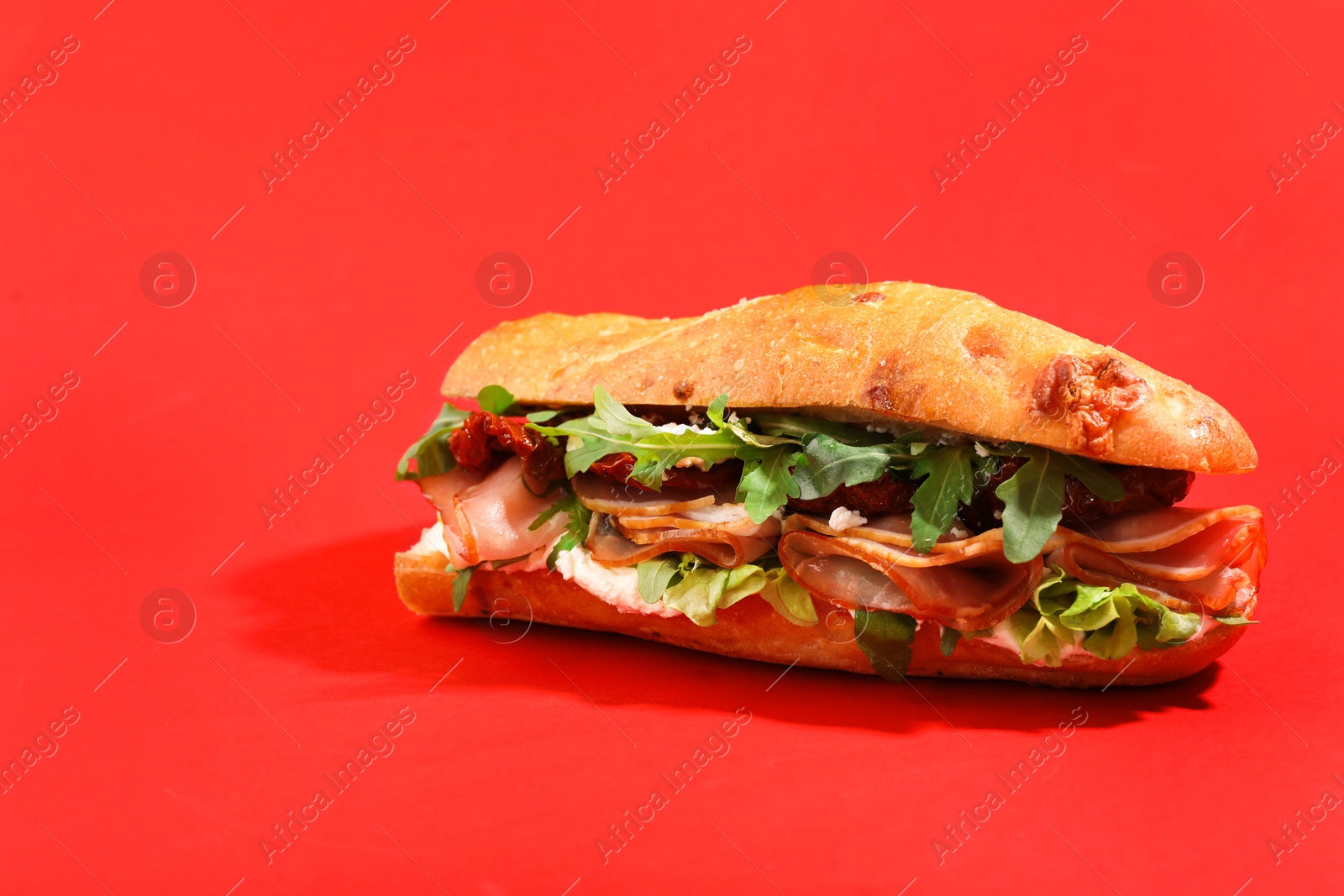 Photo of Baguette sandwich with ham and sun dried tomatoes on red background