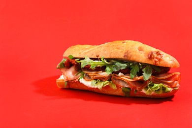 Photo of Baguette sandwich with ham and sun dried tomatoes on red background