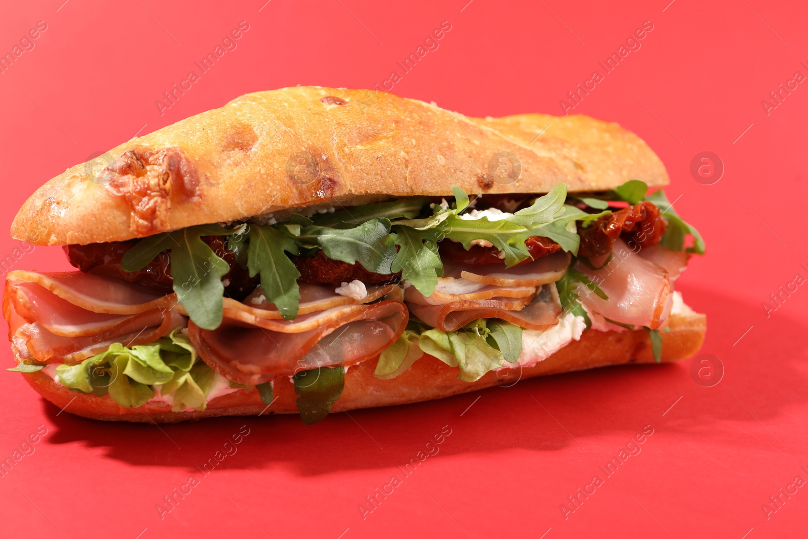 Photo of Baguette sandwich with ham and sun dried tomatoes on red background, closeup