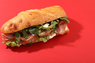 Photo of Baguette sandwich with ham and sun dried tomatoes on red background, closeup