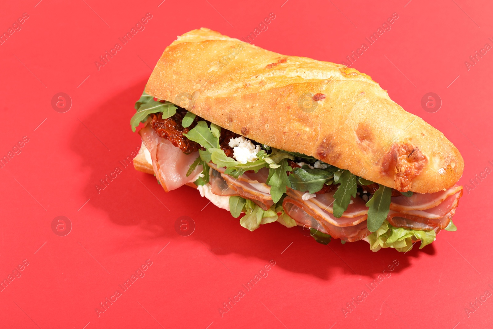 Photo of Baguette sandwich with ham and sun dried tomatoes on red background