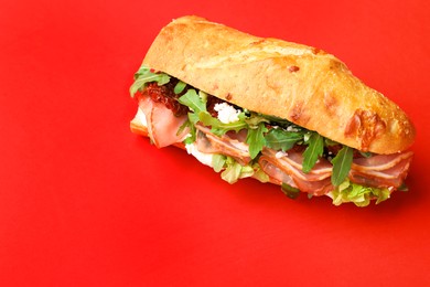 Photo of Baguette sandwich with ham and sun dried tomatoes on red background. Space for text