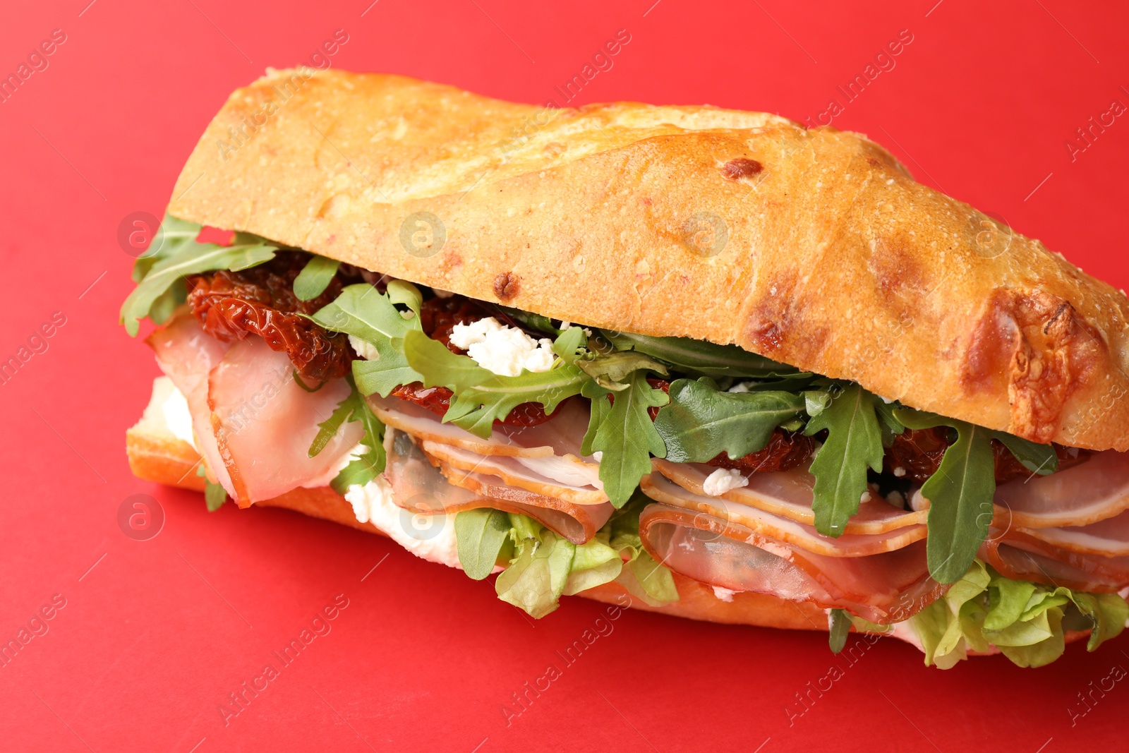 Photo of Baguette sandwich with ham and sun dried tomatoes on red background, closeup