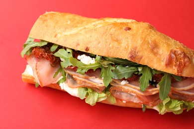 Photo of Baguette sandwich with ham and sun dried tomatoes on red background, closeup