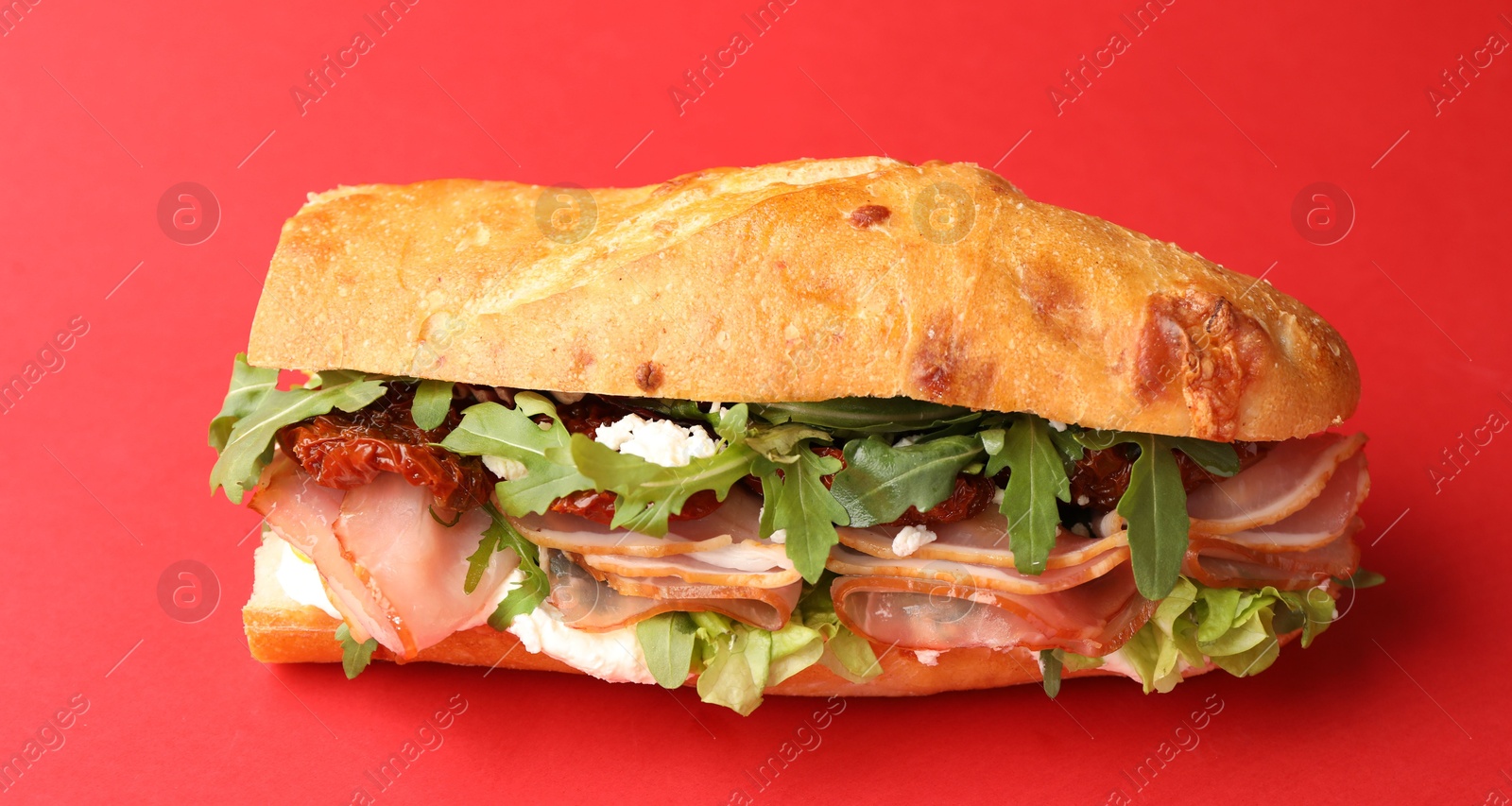 Photo of Baguette sandwich with ham and sun dried tomatoes on red background, closeup