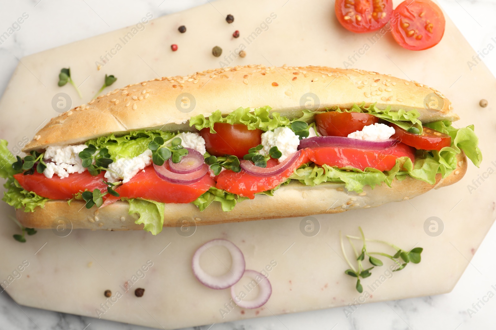 Photo of Delicious baguette with salmon on white marble table, top view