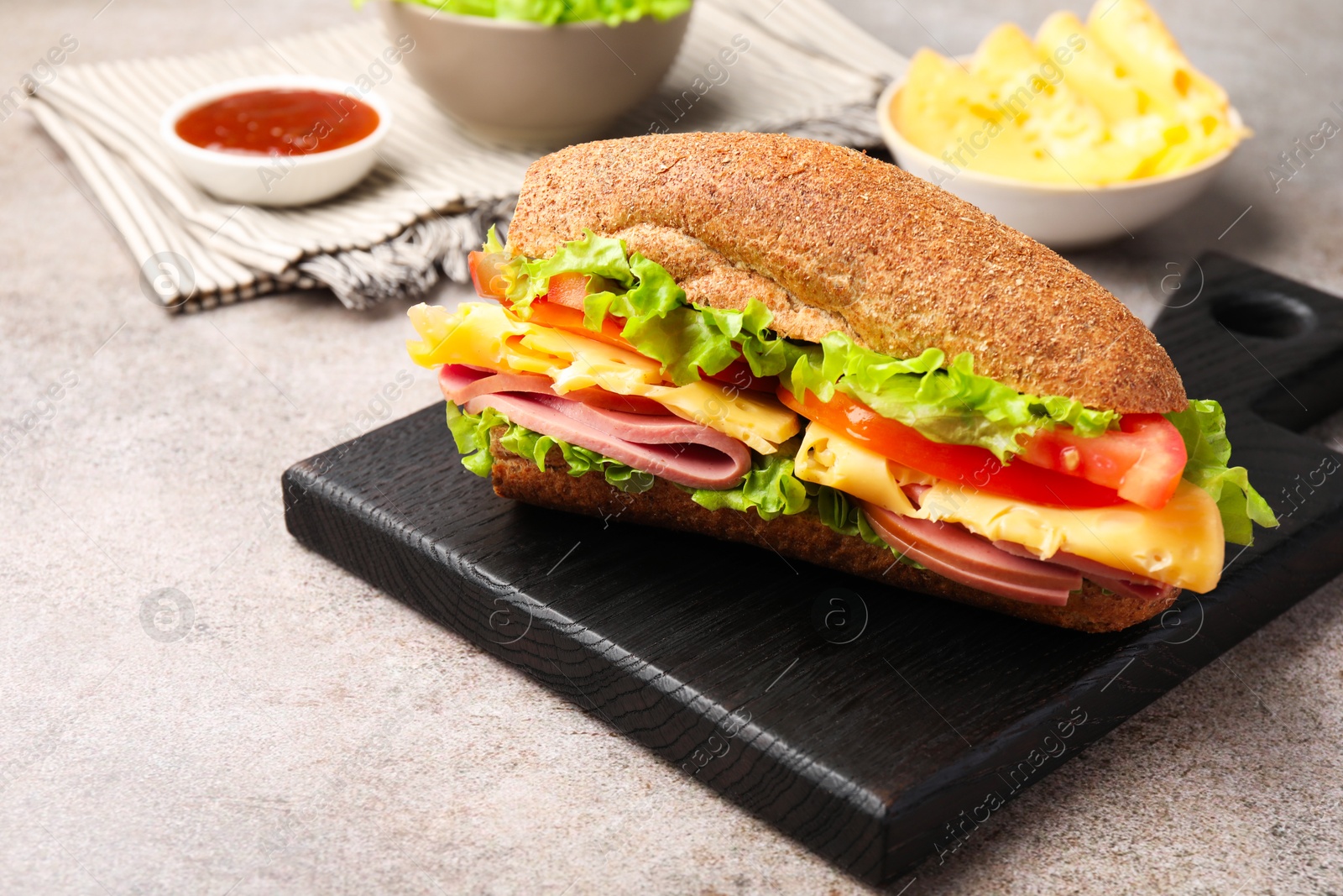 Photo of Delicious baguette sandwich with ham and ingredients on grey table