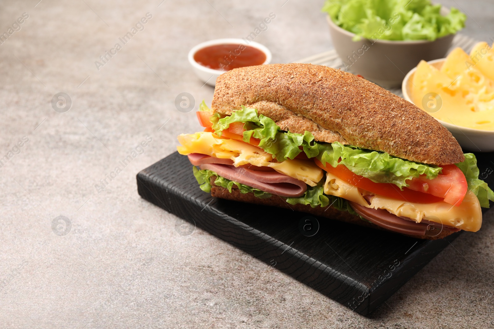 Photo of Delicious baguette sandwich with ham and ingredients on grey table