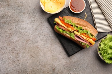 Photo of Delicious baguette sandwich with ham and ingredients on grey table, flat lay. Space for text