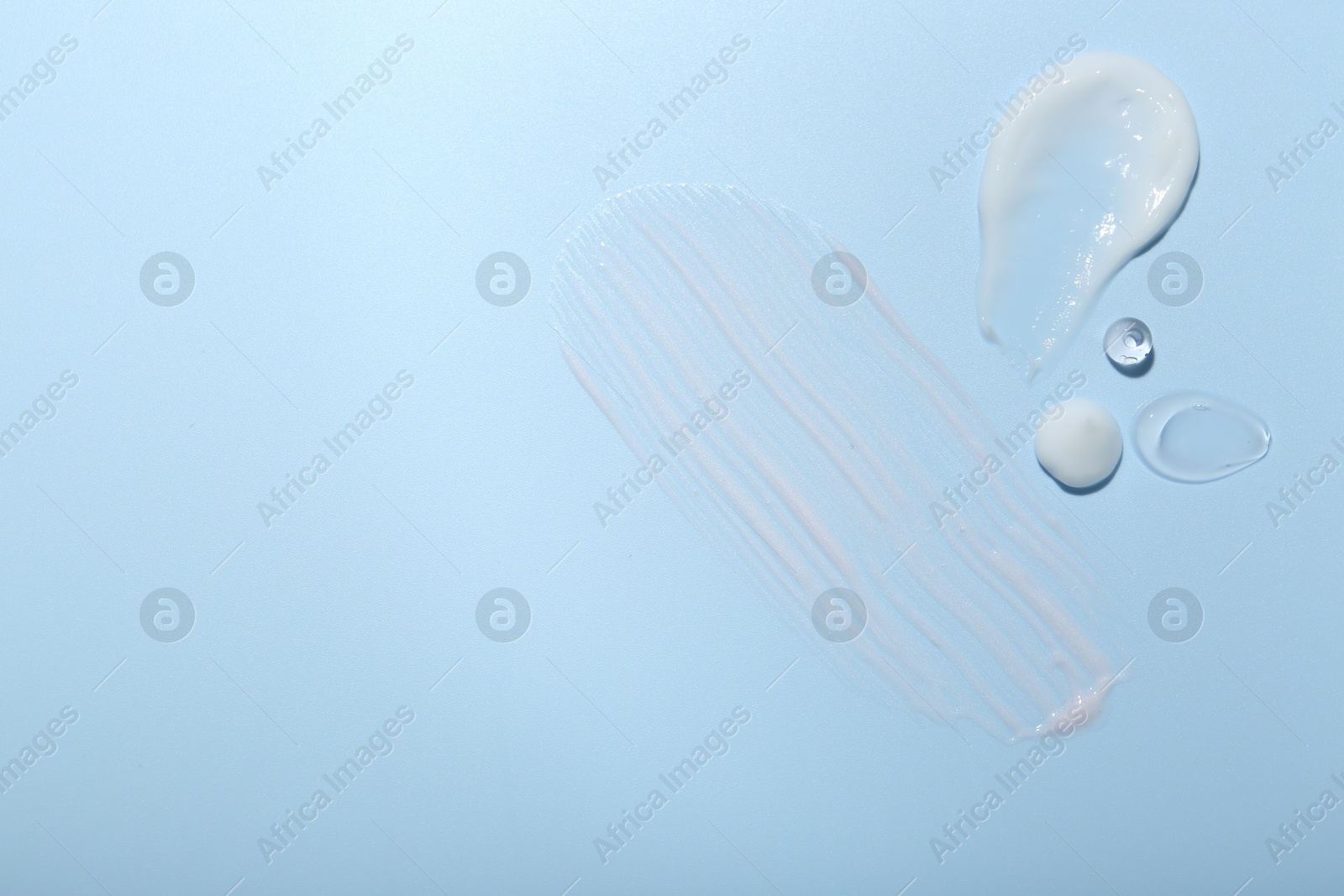 Photo of Cream and gel samples on light blue background, top view. Space for text