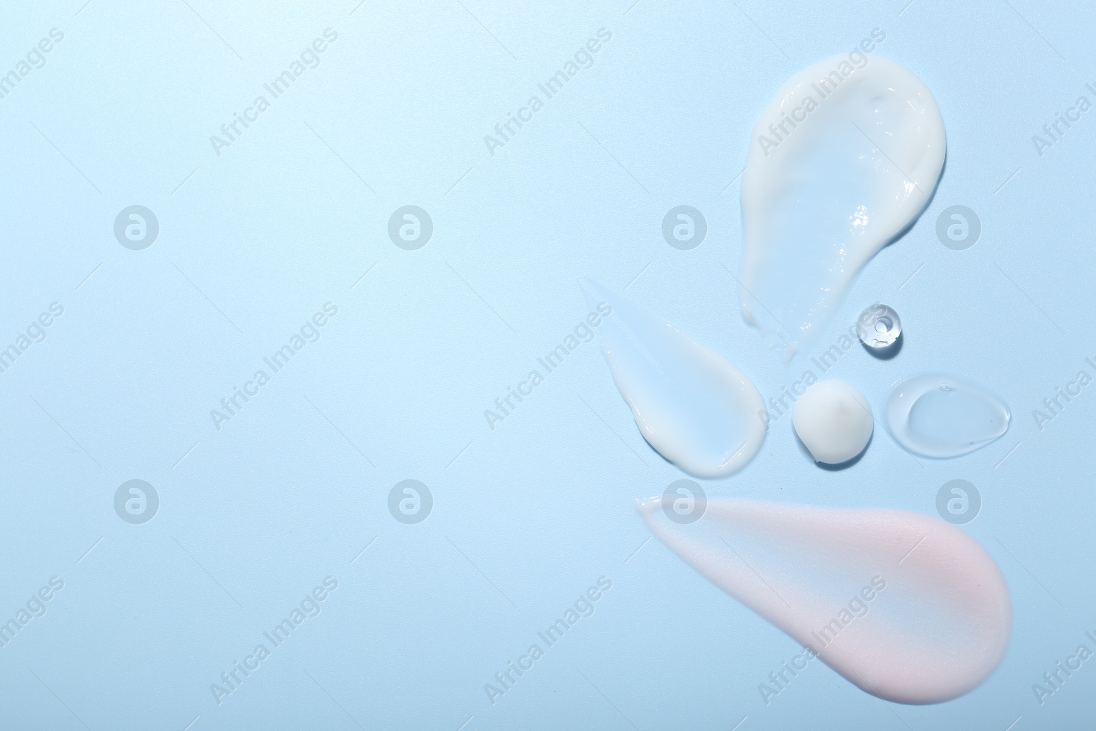 Photo of Cream and gel samples on light blue background, top view. Space for text