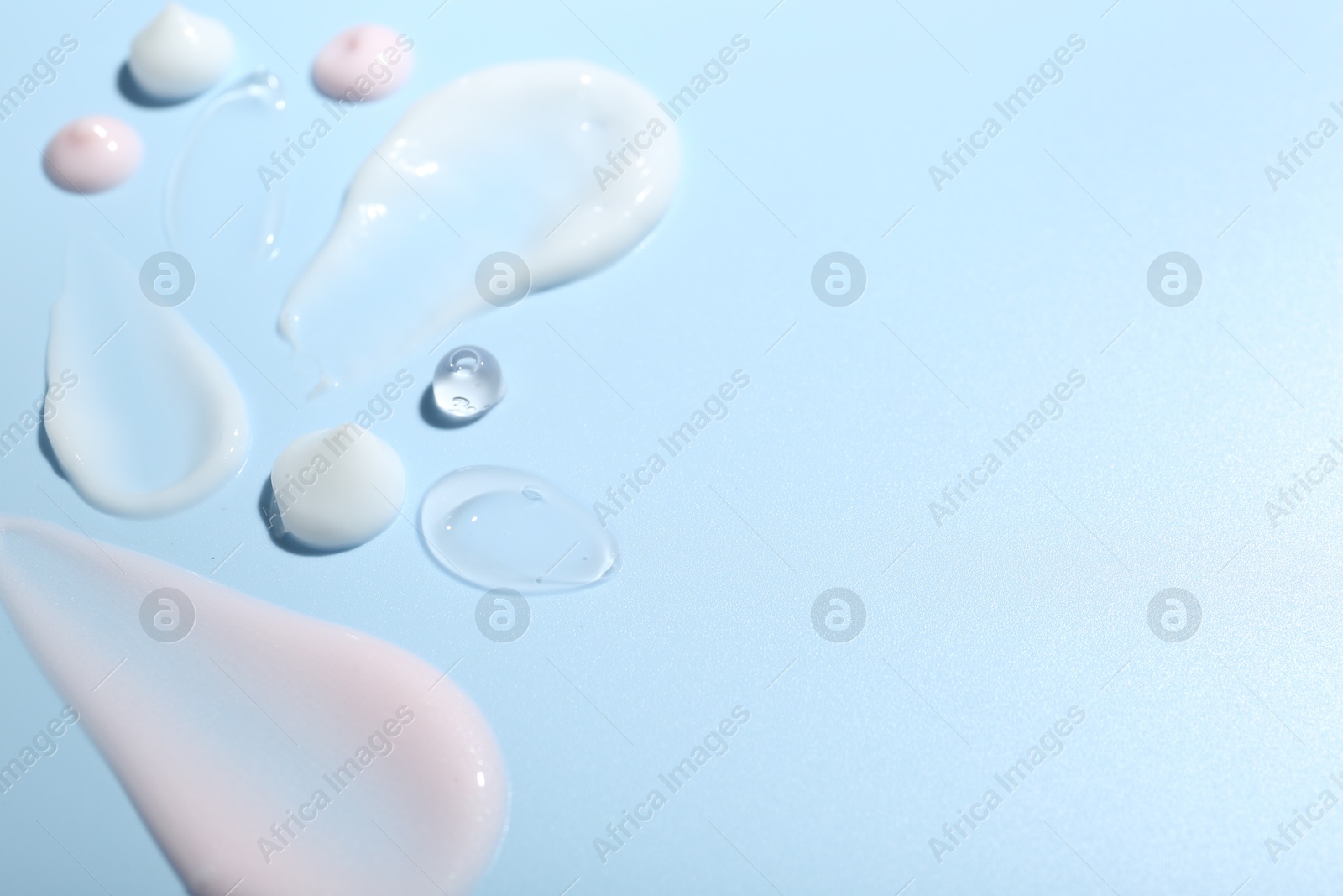 Photo of Cream and gel samples on light blue background, closeup. Space for text