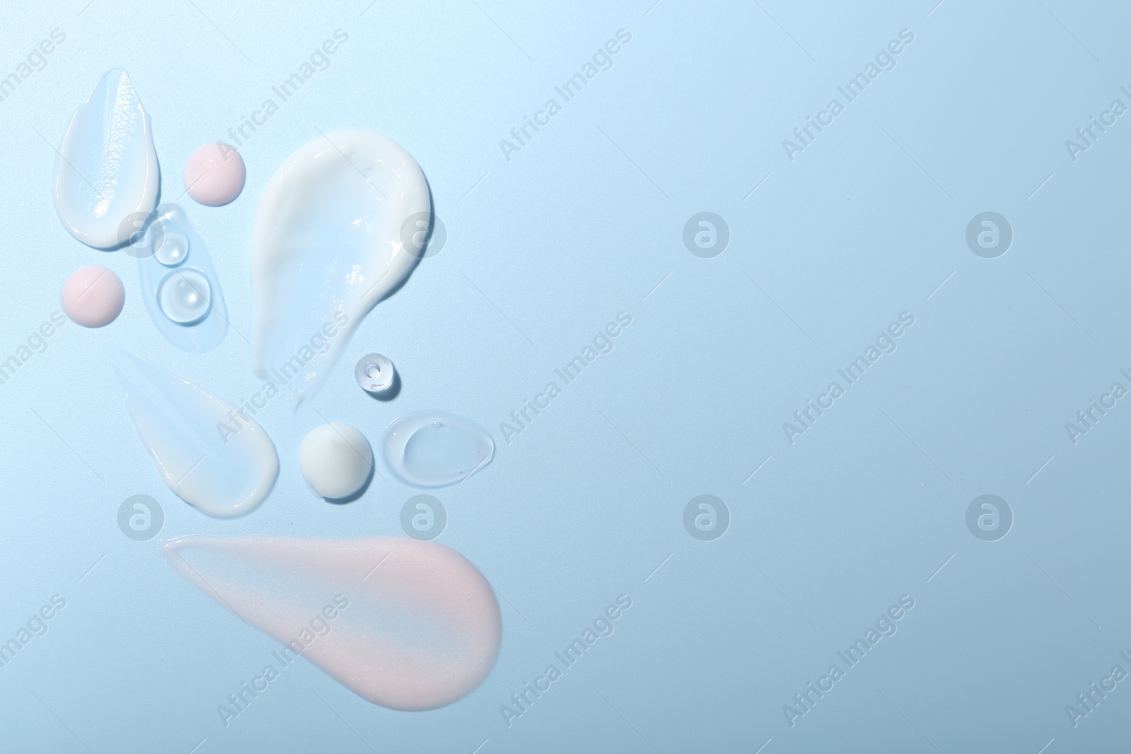 Photo of Cream and gel samples on light blue background, top view. Space for text