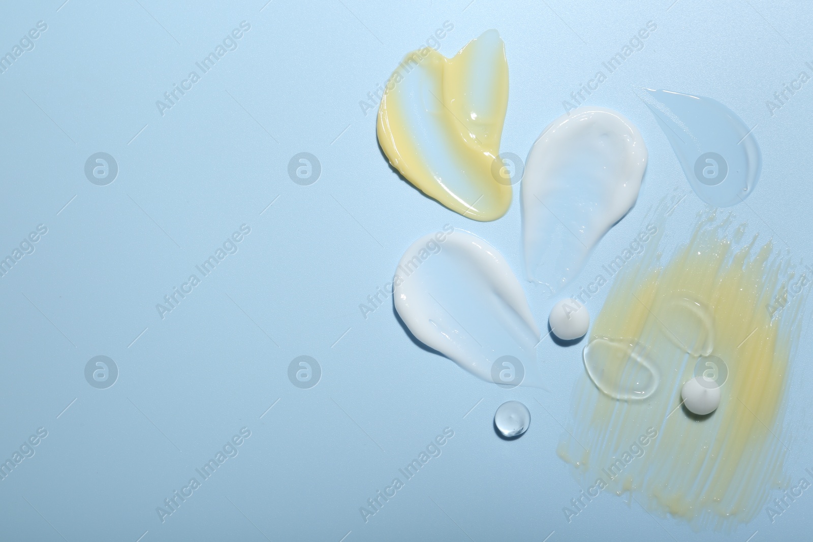 Photo of Cream and gel samples on light blue background, top view. Space for text