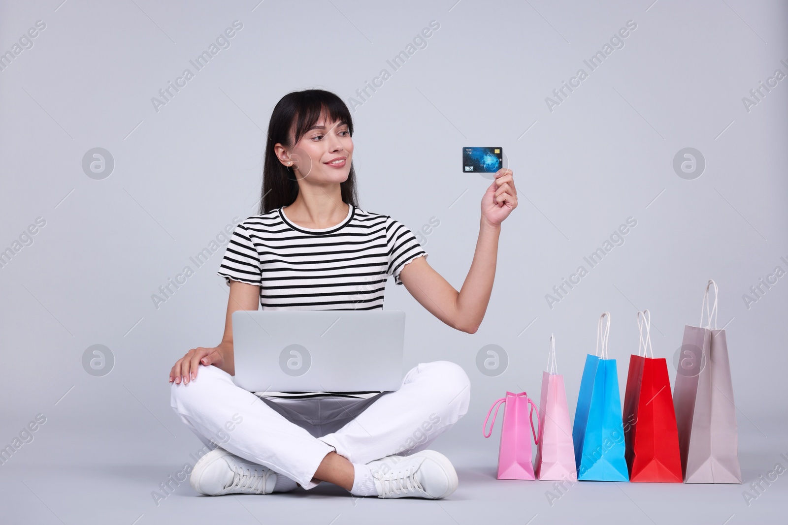 Photo of Internet shopping. Happy woman with credit card, laptop and colorful bags on grey background