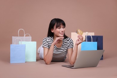 Photo of Internet shopping. Happy woman with credit card, laptop and colorful bags on beige background