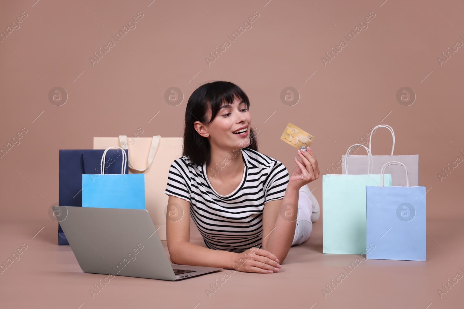 Photo of Internet shopping. Happy woman with credit card, laptop and colorful bags on beige background