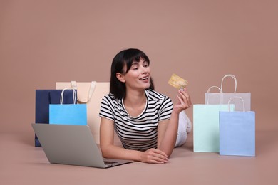 Photo of Internet shopping. Happy woman with credit card, laptop and colorful bags on beige background