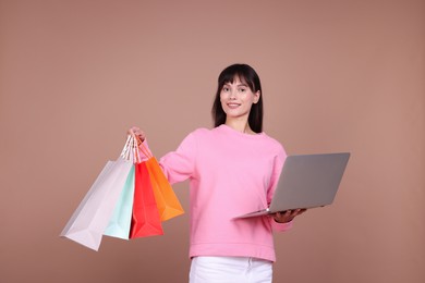 Photo of Internet shopping. Happy woman with laptop and colorful bags on beige background