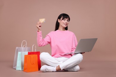 Photo of Internet shopping. Happy woman with credit card, laptop and colorful bags on beige background