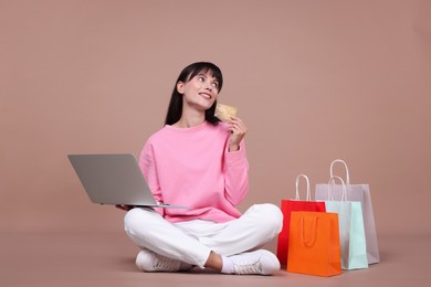 Photo of Internet shopping. Happy woman with credit card, laptop and colorful bags on beige background