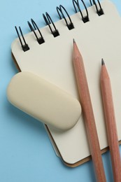 Eraser, pencils and notepad on light blue background, top view