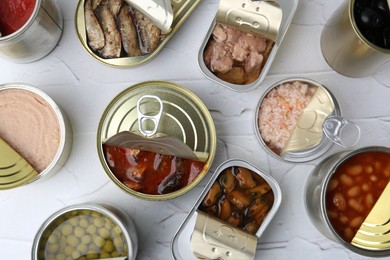 Photo of Open tin cans with different preserved products on white table, flat lay