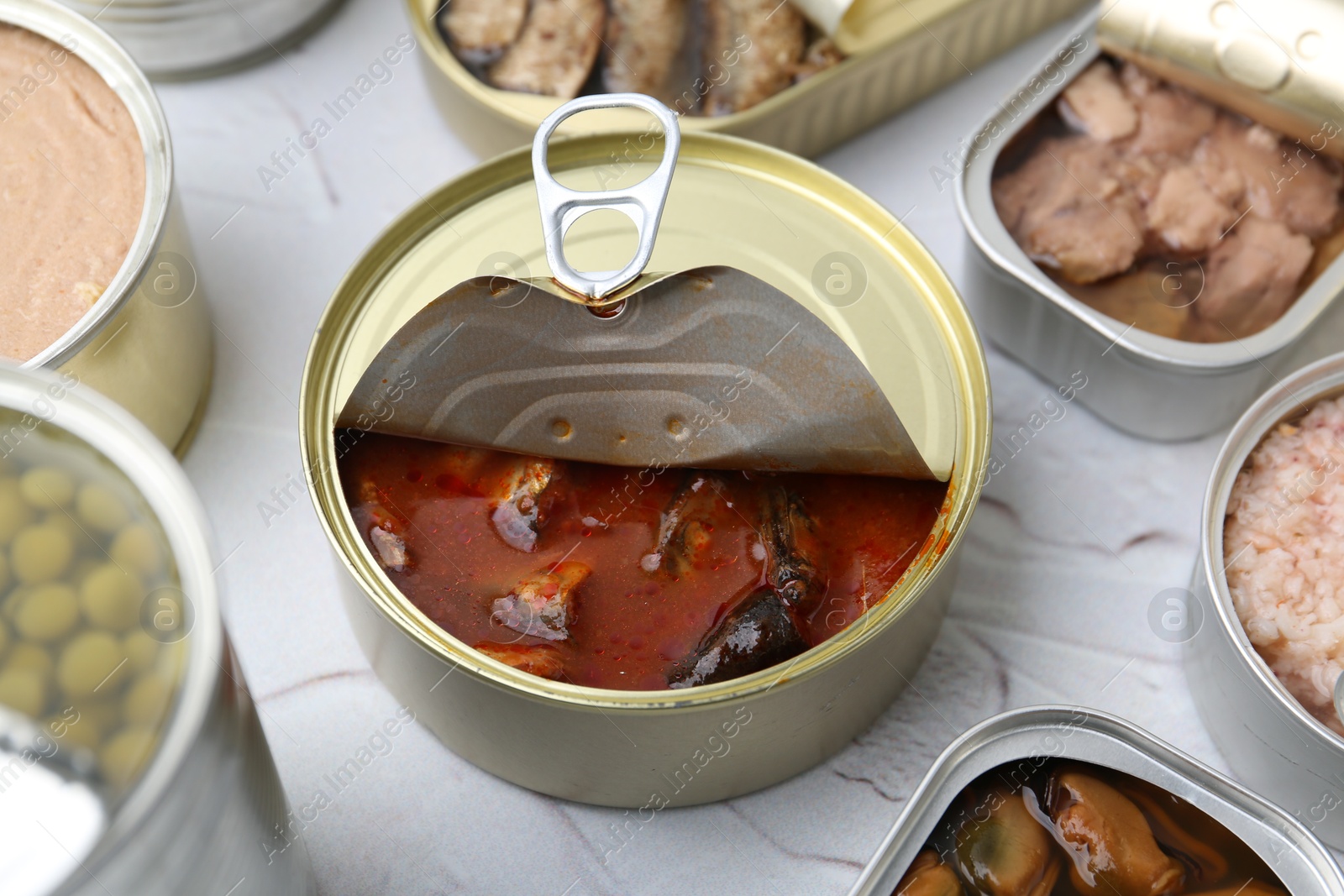 Photo of Open tin cans with different preserved products on white table, closeup