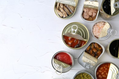 Photo of Open tin cans with different preserved products on white table, flat lay. Space for text