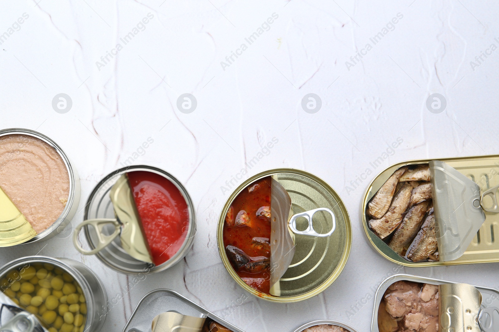 Photo of Open tin cans with different preserved products on white table, flat lay. Space for text