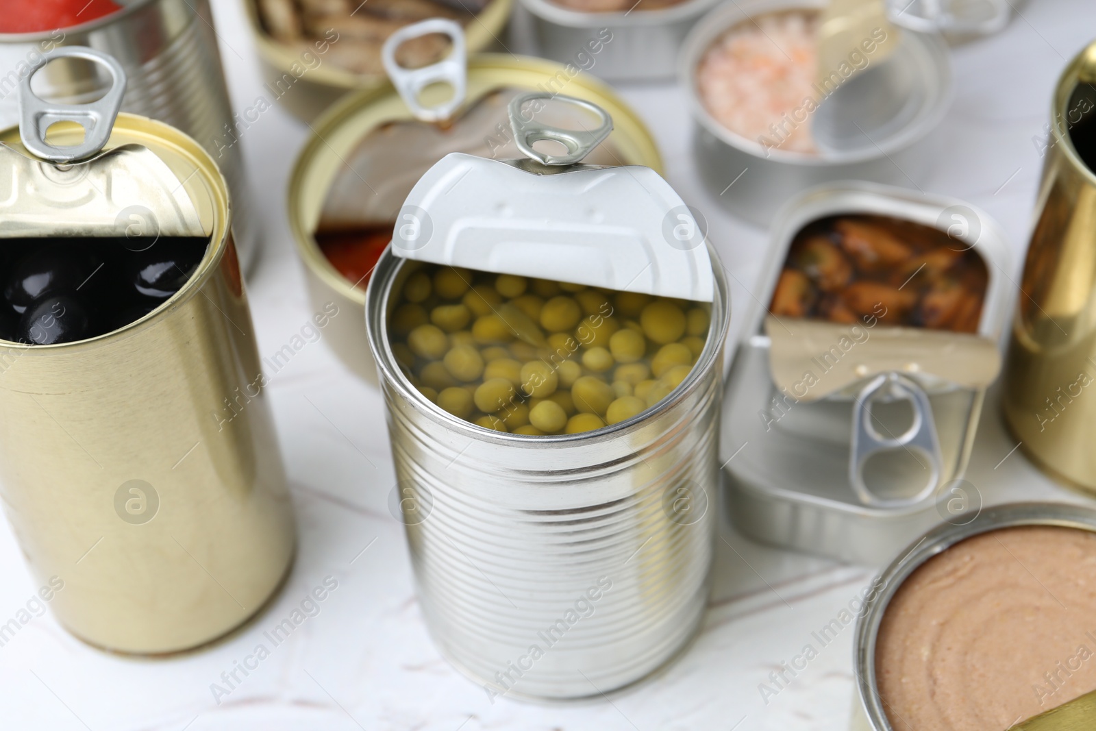 Photo of Open tin cans with different preserved products on white table, closeup