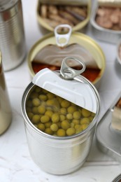 Photo of Open tin cans with different preserved products on white table, closeup