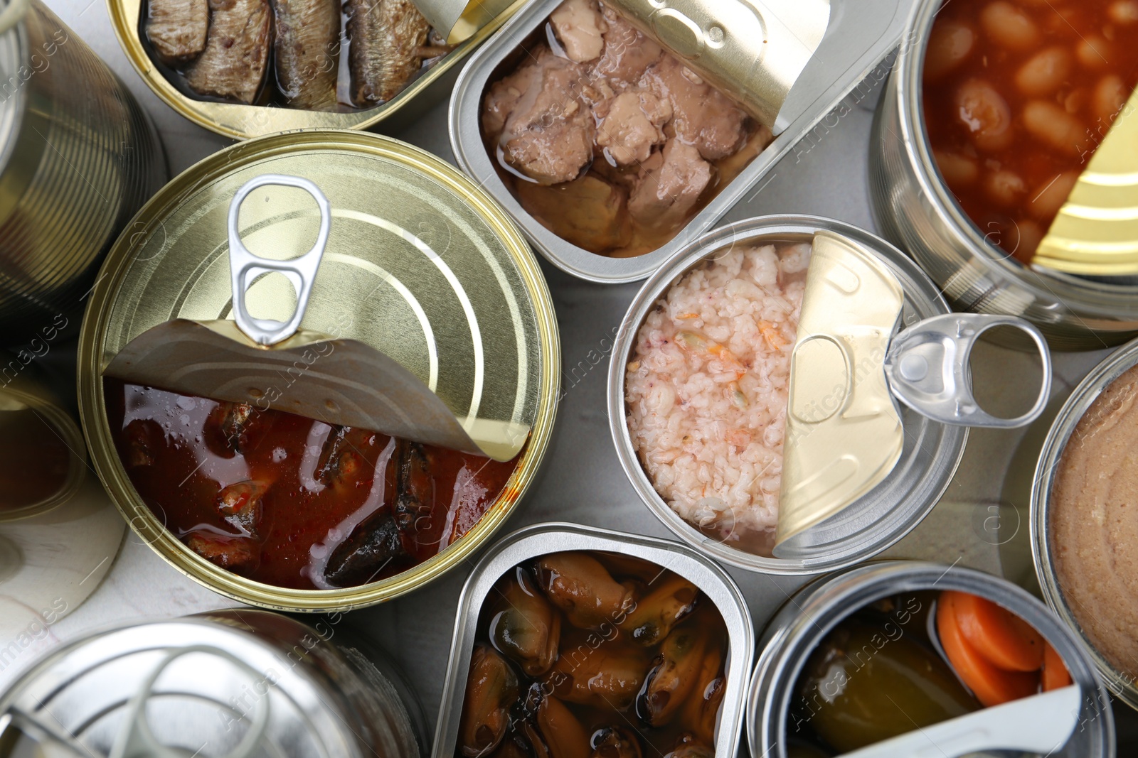 Photo of Open tin cans with different preserved products on table, flat lay