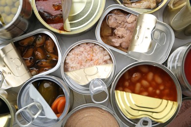 Photo of Open tin cans with different preserved products on table, flat lay