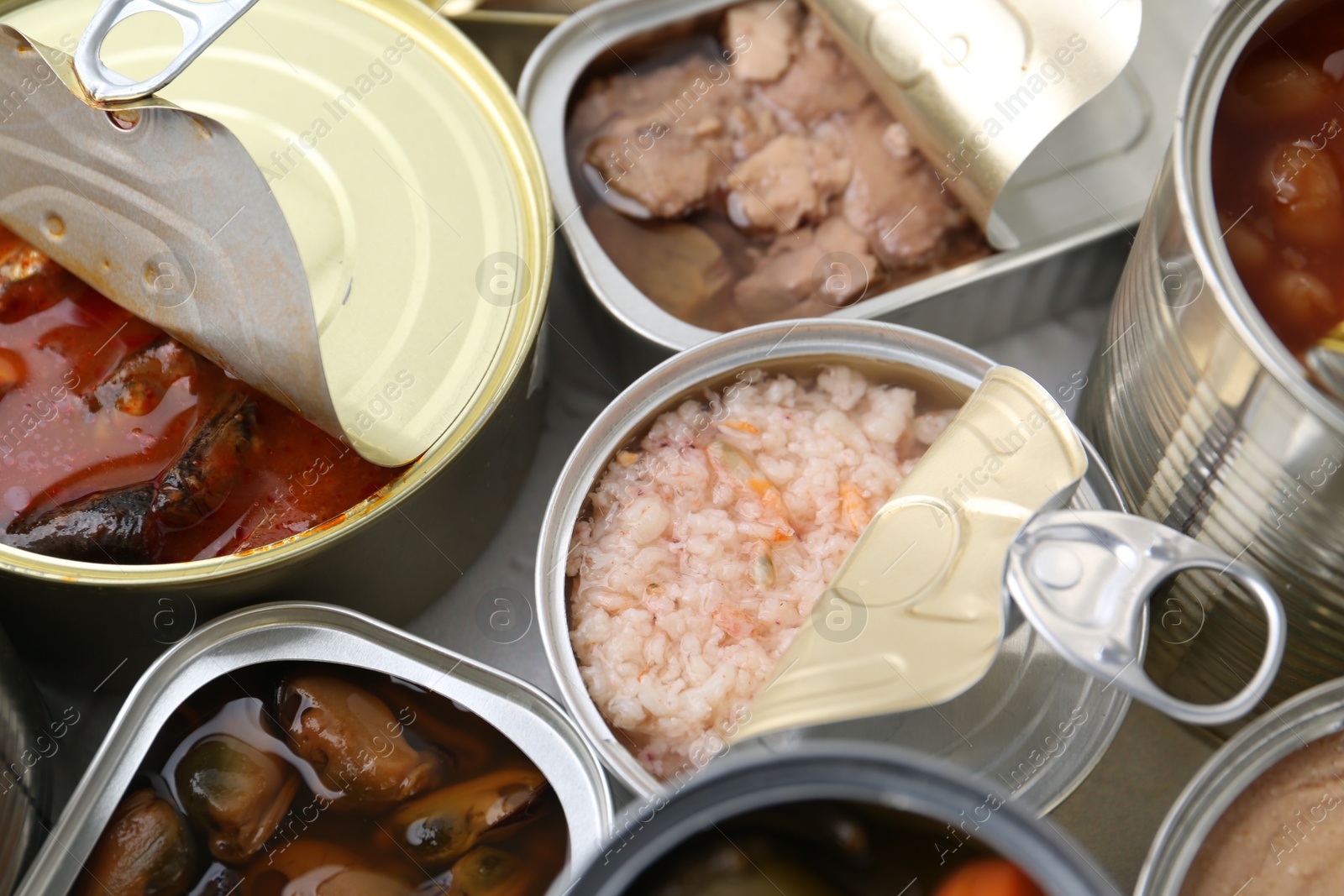 Photo of Open tin cans with different preserved products on table, closeup