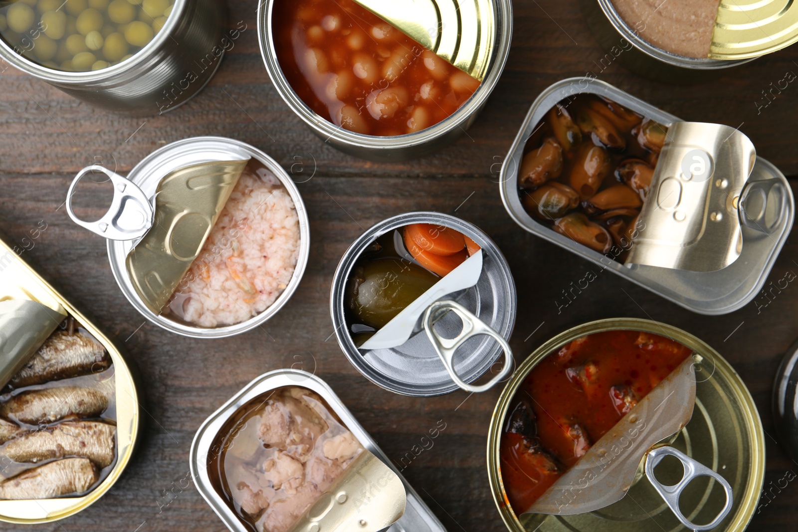 Photo of Open tin cans with different preserved products on wooden table, flat lay