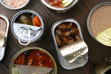 Photo of Open tin cans with different preserved products on wooden table, flat lay