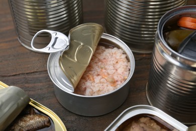 Open tin cans with different preserved products on wooden table, closeup