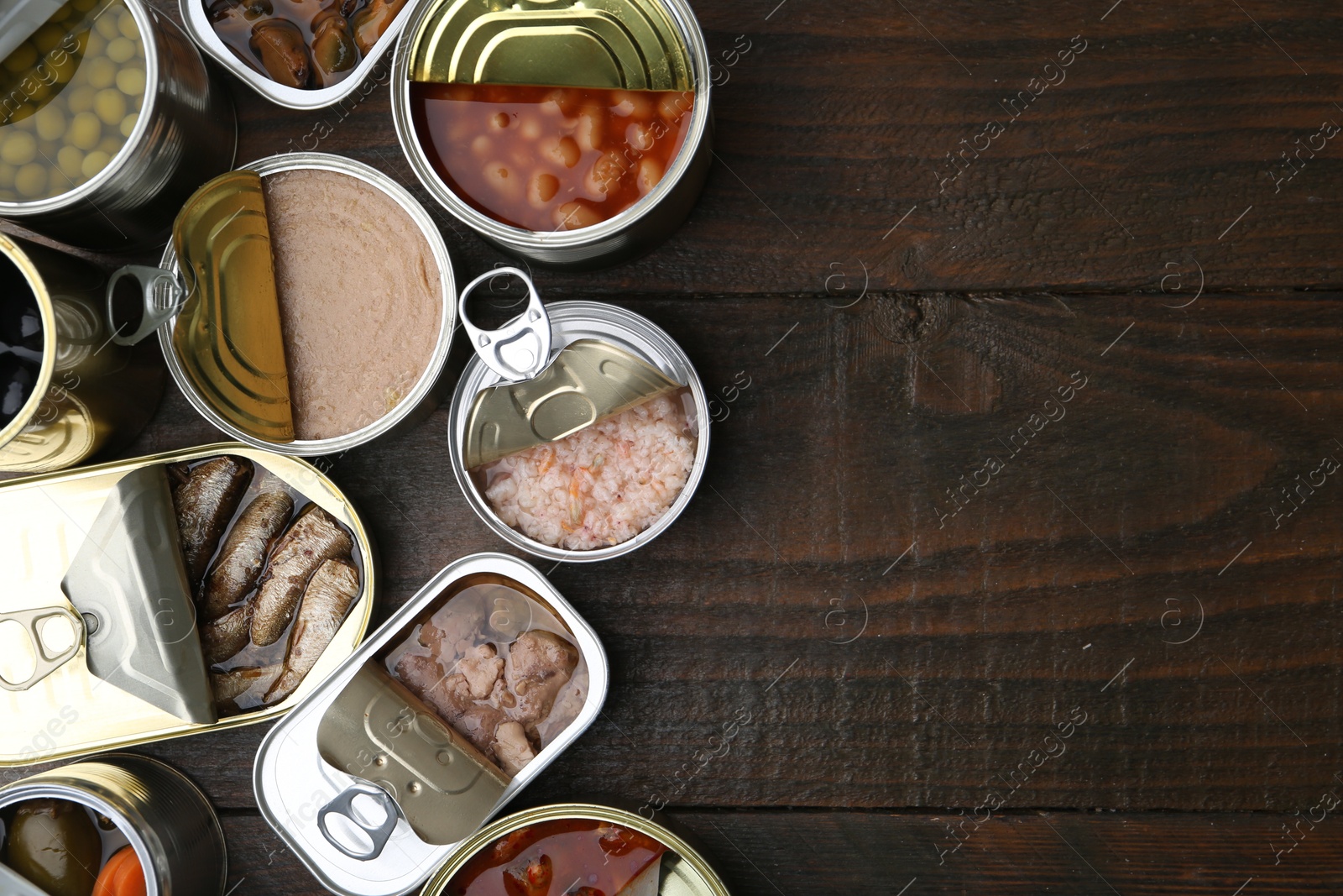 Photo of Open tin cans with different preserved products on wooden table, flat lay. Space for text