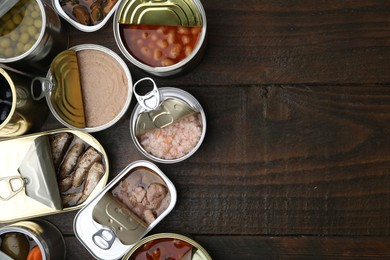 Photo of Open tin cans with different preserved products on wooden table, flat lay. Space for text