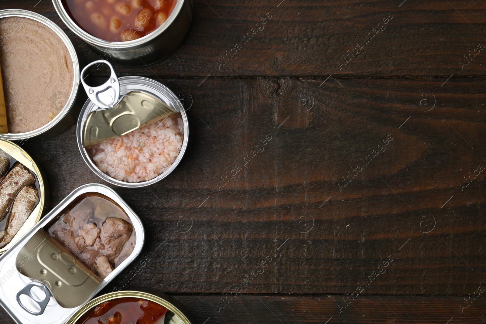 Photo of Open tin cans with different preserved products on wooden table, flat lay. Space for text