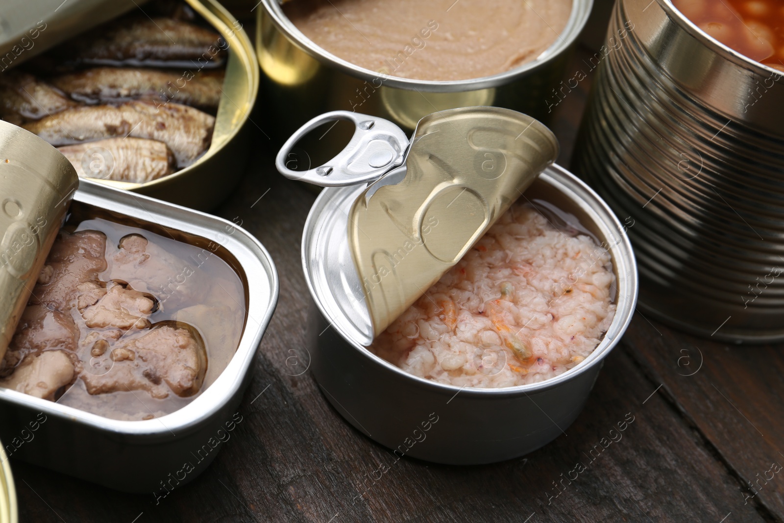 Photo of Open tin cans with different preserved products on wooden table, closeup