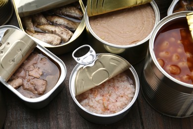 Photo of Open tin cans with different preserved products on wooden table, above view