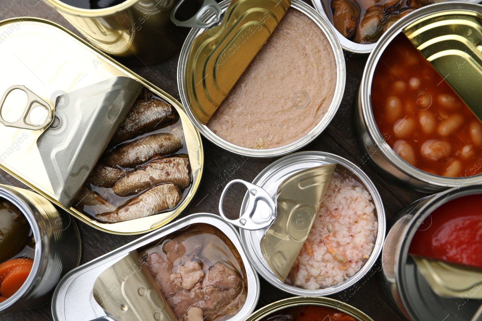 Photo of Open tin cans with different preserved products on wooden table, flat lay