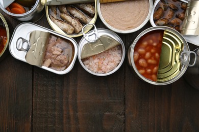 Photo of Open tin cans with different preserved products on wooden table, flat lay. Space for text