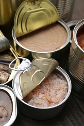 Photo of Open tin cans with different preserved products on wooden table, closeup